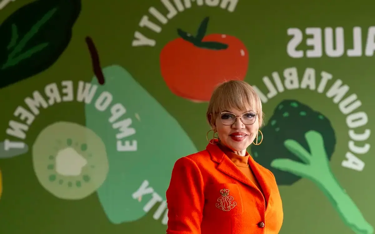 2024 Laetare winner Claire Babineaux-Fontenot, wearing an orange business suit, stands in front of a colorful wall.